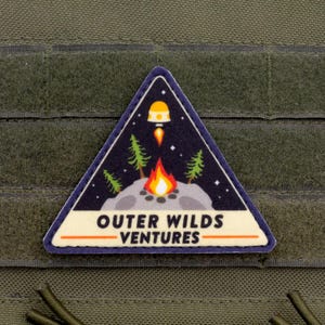 May include: A triangular patch with a space and camping theme. The patch features a rocket ship launching from a planet, a campfire, and pine trees against a starry night sky. The text "OUTER WILDS VENTURES" is displayed in white.