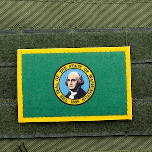 May include: A green and yellow patch featuring the Washington state flag, with a portrait of George Washington and the text "THE SEAL OF THE STATE OF WASHINGTON 1889". The patch is attached to a green fabric.