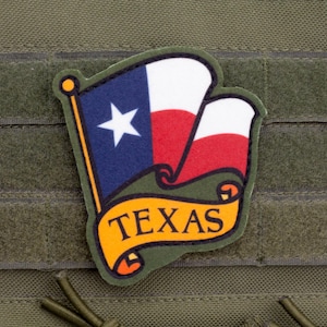 May include: A Texas flag patch featuring the state flag design with a blue field and white star, and red and white stripes. The word "TEXAS" is displayed on a yellow banner. The patch is set against a green background.