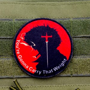 May include: A red and black round patch with a silhouette of a person with a cross and the text "You're Gonna Carry That Weight".
