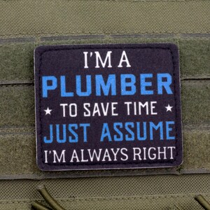 K&ouml;nnte beinhalten: Ein schwarzer und blauer Aufn&auml;her mit dem Text "I'M A PLUMBER TO SAVE TIME JUST ASSUME I'M ALWAYS RIGHT" ist auf einem gr&uuml;nen Stoff befestigt. Der Text ist in Wei&szlig; und Blau gehalten, mit Sternen.