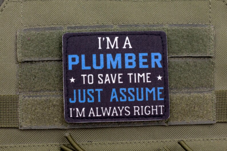K&ouml;nnte beinhalten: Ein schwarzer und blauer Aufn&auml;her mit dem Text "I'M A PLUMBER TO SAVE TIME JUST ASSUME I'M ALWAYS RIGHT" ist auf einem gr&uuml;nen Stoff befestigt. Der Text ist in Wei&szlig; und Blau gehalten, mit Sternen.