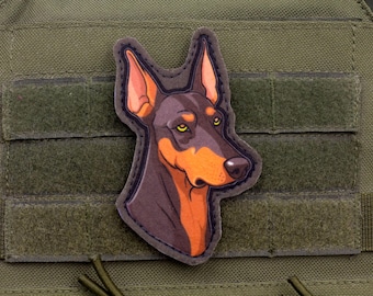 May include: A Doberman Pinscher patch with a detailed illustration of the dog's head. The patch features a brown and orange color scheme with yellow eyes and is set against a green background.