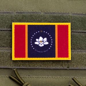 Pode incluir: Um patch retangular com a bandeira do estado do Mississippi. A bandeira tem um campo azul marinho com uma flor de magnólia branca rodeada por estrelas. Listras vermelhas verticais ladeiam o campo azul, e a bandeira é contornada em amarelo. O texto "IN GOD WE TRUST" é visível.