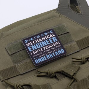May include: Olive green tactical vest with a rectangular patch. The patch reads "I'M A MECHANICAL ENGINEER I SOLVE PROBLEMS YOU DON'T KNOW YOU HAVE IN WAYS YOU CAN'T UNDERSTAND" in white and blue text.