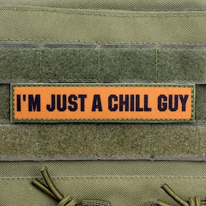 Puede incluir: Un chaleco táctico verde oliva con un parche rectangular naranja. El parche dice "I'M JUST A CHILL GUY" en letras mayúsculas negras y en negrita. El chaleco tiene cierres de velcro y correas.