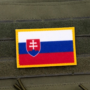 Pode incluir: Um patch retangular com a bandeira da Eslováquia, com um tricolor horizontal branco, azul e vermelho e um brasão de armas. O patch tem uma borda amarela e é fixado a um fundo de tecido verde.