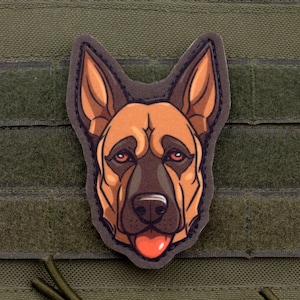 May include: A patch featuring a detailed illustration of a German Shepherd dog's head. The dog has brown and tan fur, with a pink tongue sticking out. The patch is attached to a green fabric background.
