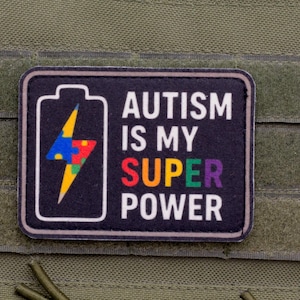 Puede incluir: Un parche rectangular negro con borde blanco que presenta un icono de batería con un rayo relleno de un patrón de piezas de rompecabezas multicolor. El texto dice AUTISM IS MY SUPER POWER con la palabra SUPER en letras multicolores.
