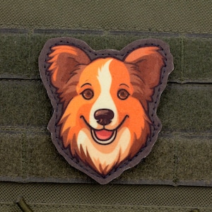 May include: A colorful patch featuring a smiling cartoon dog with orange, brown, and white fur. The patch is shaped like the dog's head and is set against a green background with a textured surface.