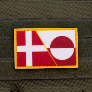 Może przedstawiać: Prostokątna naszywka z flagami Danii i Grenlandii, z żółtą obwódką. Flaga duńska to biały krzyż skandynawski na czerwonym tle. Flaga Grenlandii ma biało-czerwone koło na białym i czerwonym tle.