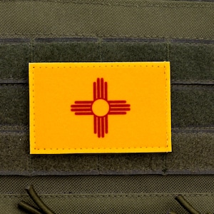 Może przedstawiać: Żółta łatka z czerwonym symbolem symbolu słońca Zia, tradycyjnym symbolem ludu Pueblo z Nowego Meksyku, na zielonym tle.