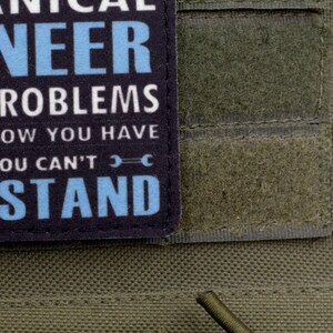 May include: A close-up of a patch with the text "MECHANICAL ENGINEER" in white and light blue. The patch is on a green fabric background. The text continues with "SOLVE PROBLEMS YOU DON'T KNOW YOU HAVE" and "IN WAYS YOU CAN'T UNDERSTAND".