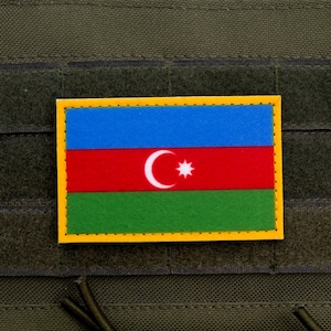 May include: A rectangular patch featuring the flag of Azerbaijan, with a blue upper section, a red middle section with a white crescent and star, and a green lower section. The patch has a yellow border and is set against a dark green background.