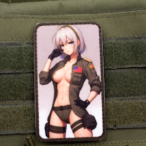 Op de afbeelding: Een anime-personage met wit haar dat een groene militaire jas draagt met een patch op de mouw. Het personage draagt een zwarte handschoen aan de ene hand en heeft een serieuze uitdrukking.
