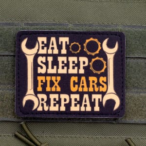May include: A rectangular black patch with rounded corners featuring the text EAT SLEEP FIX CARS REPEAT in orange and cream lettering. The design includes two vertical wrenches on the sides and two small gear icons between the words.