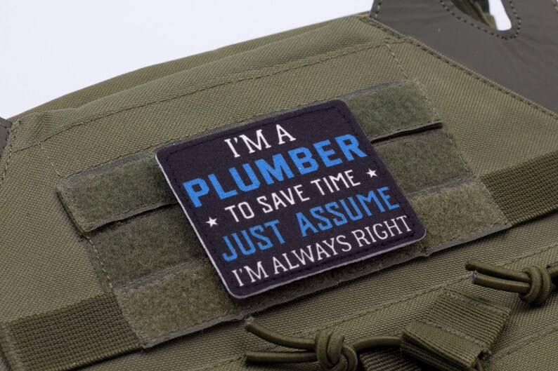 K&ouml;nnte beinhalten: Ein quadratischer Aufn&auml;her mit dem Text "I'M A PLUMBER TO SAVE TIME JUST ASSUME I'M ALWAYS RIGHT" in wei&szlig;er und blauer Schrift. Der Aufn&auml;her befindet sich auf einer gr&uuml;nen taktischen Weste.