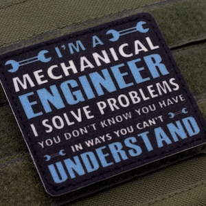 May include: A square patch with the text "I'M A MECHANICAL ENGINEER I SOLVE PROBLEMS YOU DON'T KNOW YOU HAVE IN WAYS YOU CAN'T UNDERSTAND" in white and blue on a navy blue background. The patch is on a green fabric.