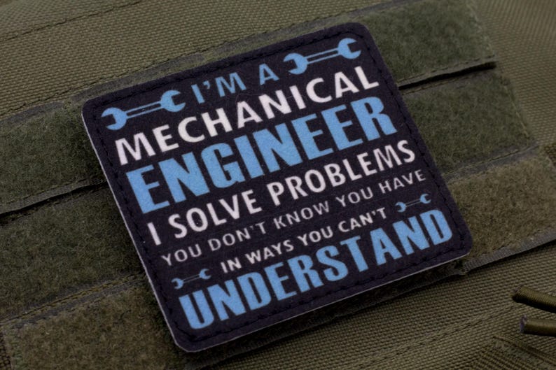 May include: A square patch with the text "I'M A MECHANICAL ENGINEER I SOLVE PROBLEMS YOU DON'T KNOW YOU HAVE IN WAYS YOU CAN'T UNDERSTAND" in white and blue on a navy blue background. The patch is on a green fabric.