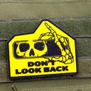 May include: A yellow and black patch featuring a skull design and the text "DON'T LOOK BACK". The patch is attached to a green tactical vest. The patch has a distinctive shape.