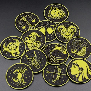 Puede incluir: Una colección de doce posavasos circulares con símbolos del zodiaco y constelaciones en amarillo brillante sobre un fondo negro. Cada posavasos muestra un signo astrológico distinto, incluyendo el toro, el cangrejo, el escorpión y los peces.