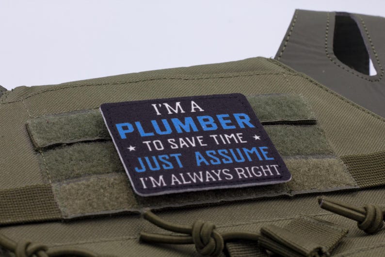 K&ouml;nnte beinhalten: Ein quadratischer Aufn&auml;her mit dem Text "I'M A PLUMBER TO SAVE TIME JUST ASSUME I'M ALWAYS RIGHT" in wei&szlig;er und blauer Schrift auf schwarzem Hintergrund. Der Aufn&auml;her ist an einer gr&uuml;nen taktischen Weste befestigt.