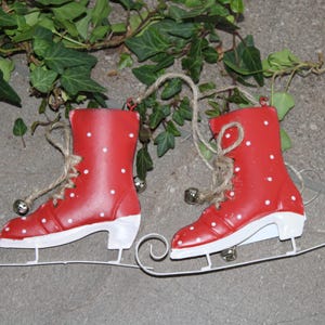 Puede incluir: Un par de patines de hielo rojos con lunares blancos y suelas blancas. Los patines est&aacute;n unidos a patines de trineo blancos. Cada pat&iacute;n tiene una cuerda de yute para colgar y una peque&ntilde;a campana plateada. Decoraci&oacute;n navide&ntilde;a.