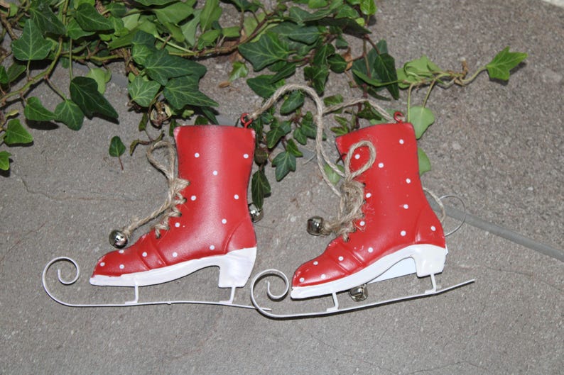 Puede incluir: Un par de patines de hielo rojos con lunares blancos y suelas blancas. Los patines est&aacute;n unidos a patines de trineo blancos. Cada pat&iacute;n tiene una cuerda de yute para colgar y una peque&ntilde;a campana plateada. Decoraci&oacute;n navide&ntilde;a.