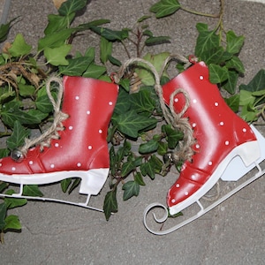 Puede incluir: Dos patines de hielo decorativos rojos con lunares blancos y cuchillas blancas. Los patines est&aacute;n atados con hilo y se encuentran entre hiedra verde.
