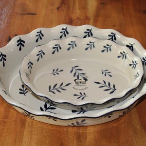 Könnte beinhalten: Zwei ineinander verschachtelte runde Keramik-Backformen mit gewelltem Rand, cremefarbener Basis und dunkelblauem Blattmuster. In der Mitte der kleineren Form befindet sich ein Kronenlogo mit dem Text Hand Painted und M.H.P. England.
