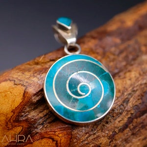 May include: A silver pendant with a turquoise spiral design. The pendant is round and has a silver bail.