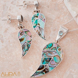 Könnte beinhalten: Ein Set aus silbernen Ohrringen und einer Halskette mit einem Blattdesign aus irisierendem Abalone-Muschelinlay. Die Ohrringe sind im Hänge-Stil mit einem kleinen schwarzen Stein oben. Die Halskette hat einen Anhänger mit einem größeren Abalone-Muschel-Blatt und einem blauen Stein oben.