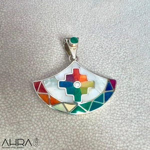 May include: A silver pendant with a colorful geometric design. The pendant is made of mother of pearl and other stones, and features a cross in the center. The pendant is attached to a silver chain.