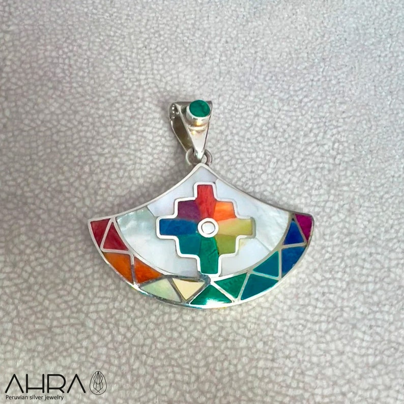 May include: A silver pendant with a colorful geometric design. The pendant is made of mother of pearl and other stones, and features a cross in the center. The pendant is attached to a silver chain.