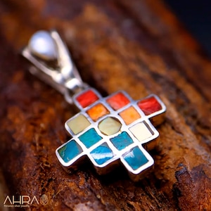 May include: A silver pendant with a colorful geometric design. The pendant is made of silver and features a variety of stones, including turquoise, coral, and mother-of-pearl. The pendant is in the shape of a cross.
