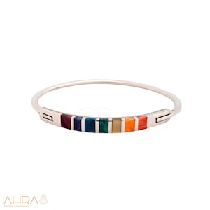 May include: A silver bangle bracelet with a colorful inlay of gemstones. The stones are arranged in a rainbow pattern, with red, orange, yellow, green, blue, indigo, and violet.