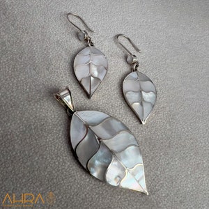 May include: A set of silver earrings and a pendant featuring a leaf design made with mother of pearl. The leaf is white with a silver outline.