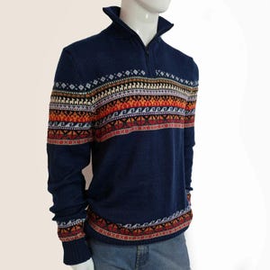 May include: A navy blue sweater with a half-zip collar and a colorful patterned design across the chest and sleeves. The pattern includes geometric shapes and stylized animal figures in shades of red, orange, and white.
