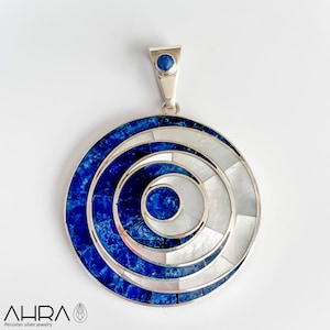 May include: A silver pendant with a circular design featuring concentric circles of blue lapis lazuli and white mother-of-pearl. The pendant has a small blue lapis lazuli stone at the top.
