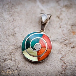 May include: A silver pendant with a circular design featuring a spiral of colorful stones, including turquoise, red, and white. The pendant is attached to a silver bail with a small white stone.