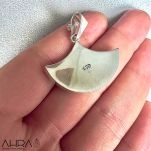May include: Silver pendant with a crescent moon shape. The back of the pendant is stamped with "950".