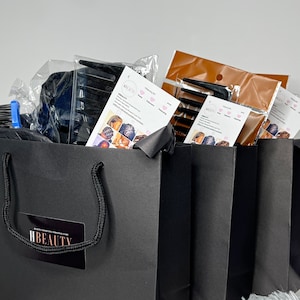 May include: Three black shopping bags with white handles. The bags have a logo that says "H BEAUTY" in white text on a black background. The bags are filled with various items, including combs, hair ties, and packaging.