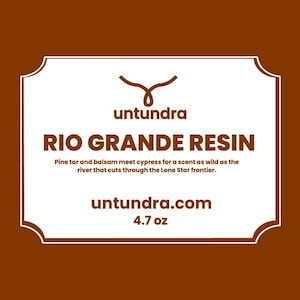 May include: A white label with a brown border and a brown logo. The label reads "untundra" and "RIO GRANDE RESIN". The text below the title reads "Pine tar and balsam meet cypress for a scent as wild as the river that cuts through the Lone Star frontier." The bottom of the label reads "untundra.com" and "4.7 oz".