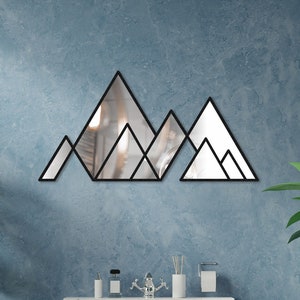 May include: A white bathtub with a geometric mountain mirror above it. The mirror is made of black metal and has a reflective surface. There are two green plants in pots on either side of the bathtub.