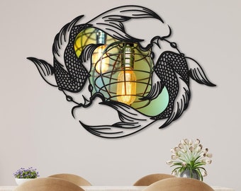 May include: Black metal wall art featuring two stylized koi fish swimming in a circle. The fish are facing each other and their tails are intertwined. The art is mounted on a white wall above a dining table with two chairs.