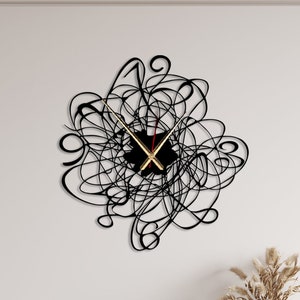 May include: Black wall clock with gold hands and a black face. The clock is in the shape of a circle and has a design of black lines that look like scribbles. The clock is hanging on a white wall above a black and white dresser.