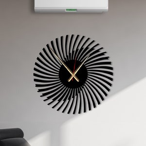 Puede incluir: Un reloj de pared negro y dorado con un diseño en espiral. Las manecillas del reloj son doradas y rojas.