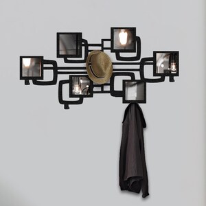 May include: Black metal wall-mounted coat rack with a geometric design featuring multiple rectangular mirrors. A hat and a jacket are hanging on the rack.