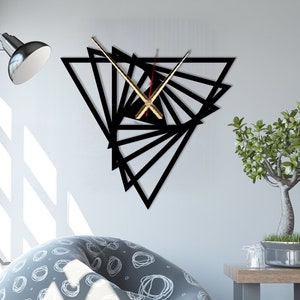 May include: A black geometric wall clock with gold hands. The clock is in the shape of a triangle and is made up of overlapping triangles. The clock is hanging on a white wall in a living room setting.