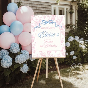 Puede incluir: Un cartel de bienvenida rosa y blanco con una cinta azul y un diseño floral. El cartel dice "Bienvenido a Eloise's Fancy 1st Birthday".